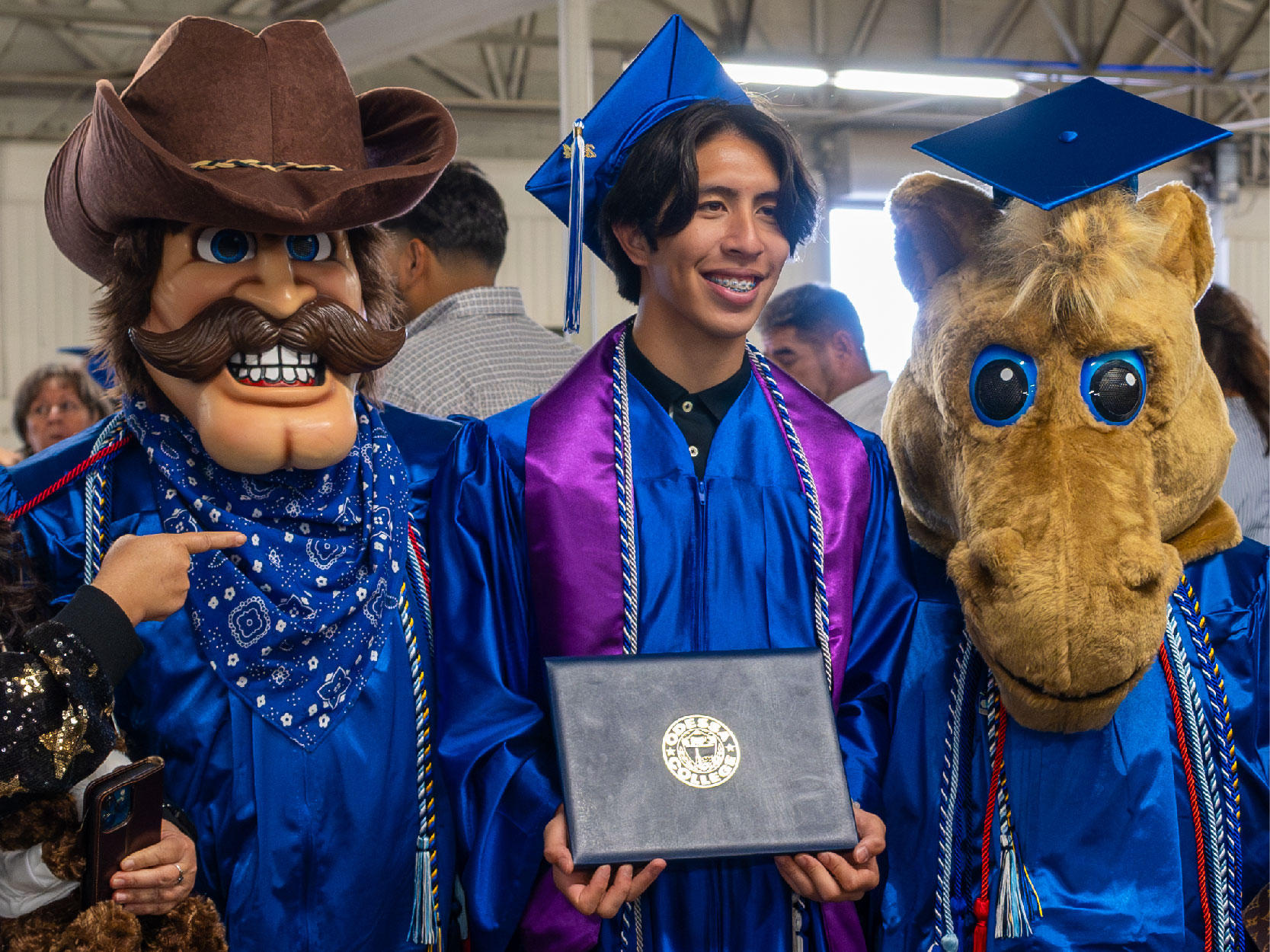 Male Graduate Posing with Willie the Wrangler and Bullseye Billie Mascots