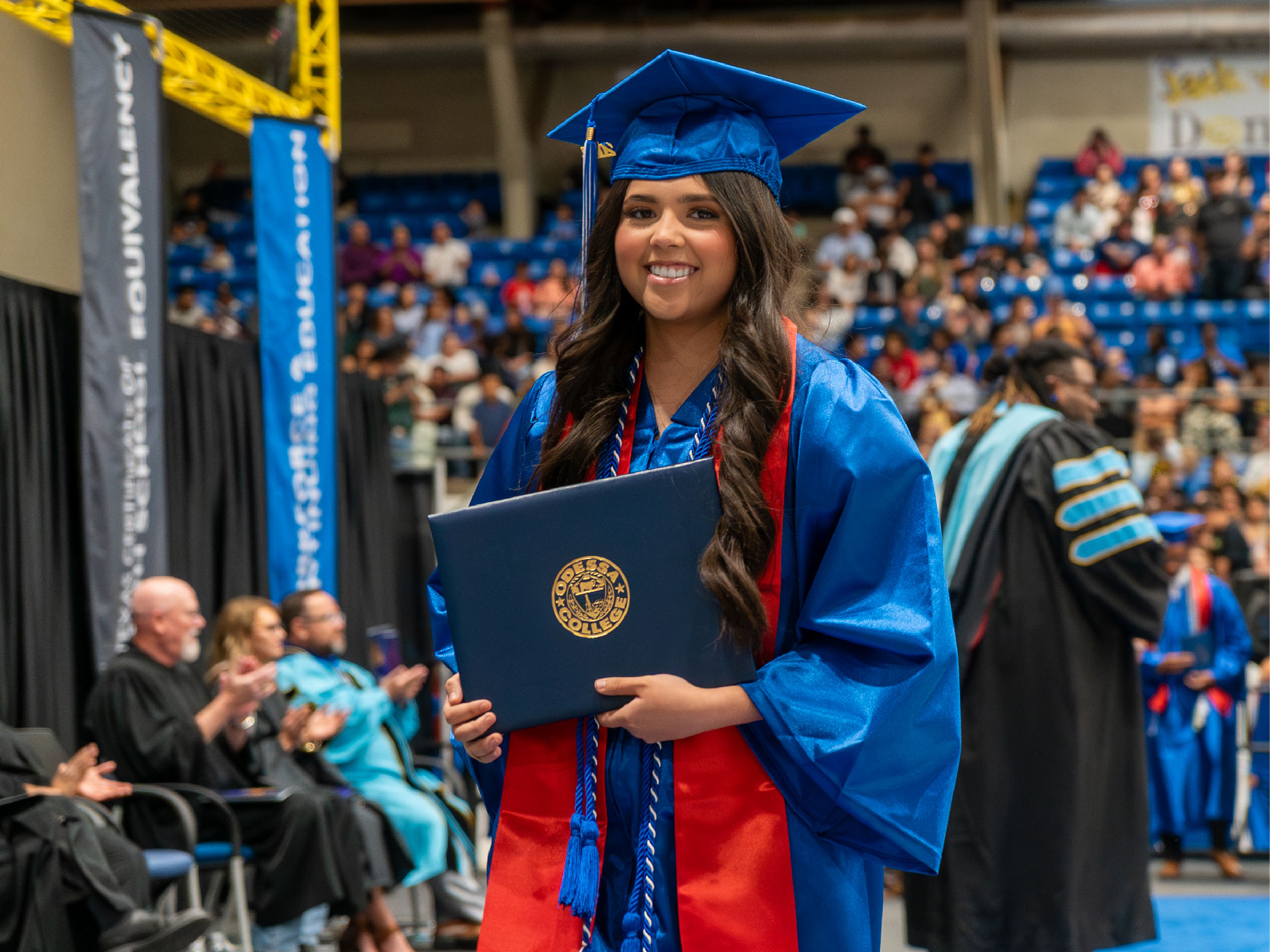 Brunette Female in Blue Cap and Gown Holding Diploma