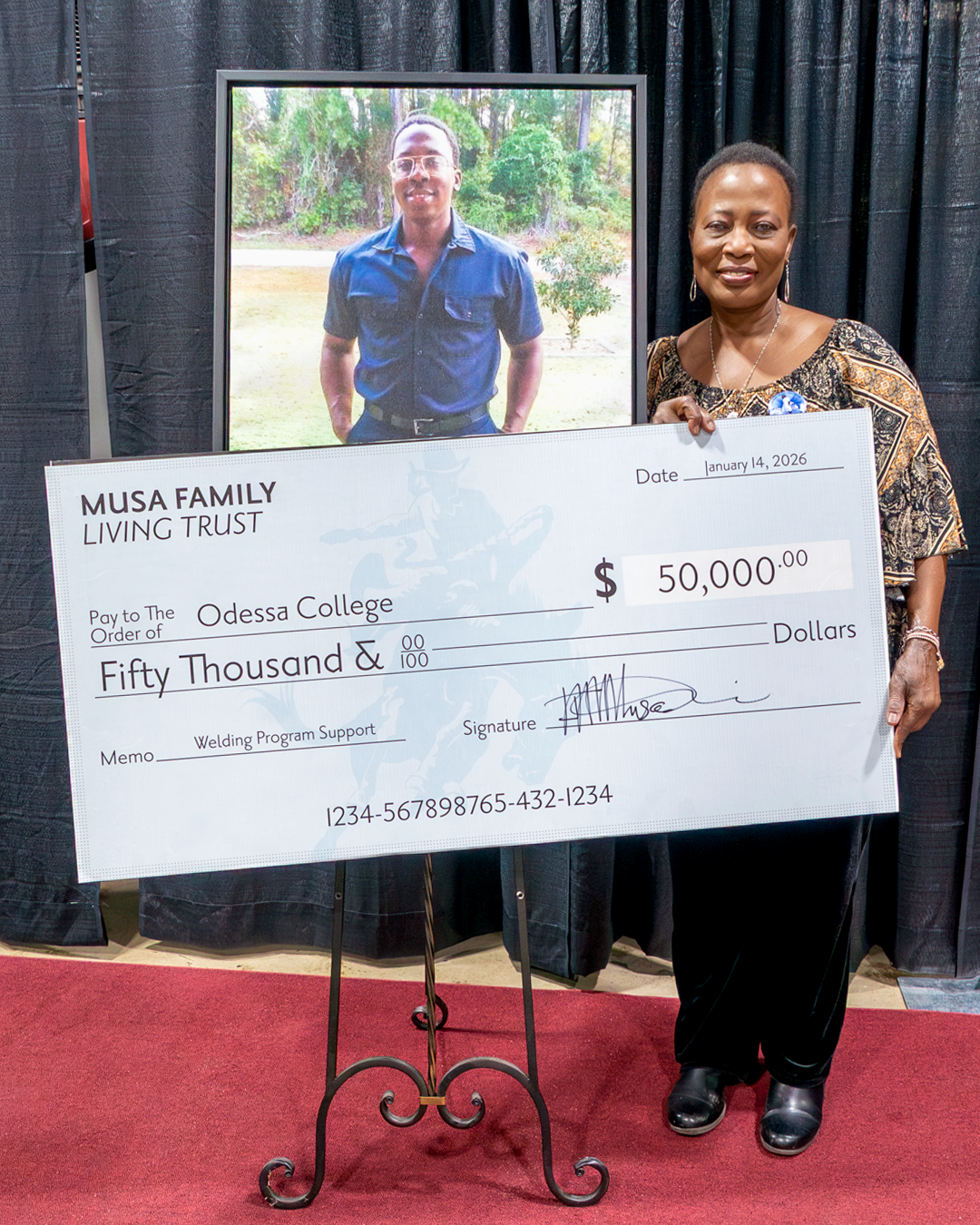 Ms. Musa holds a check while standing in front of a photograph of her late son
