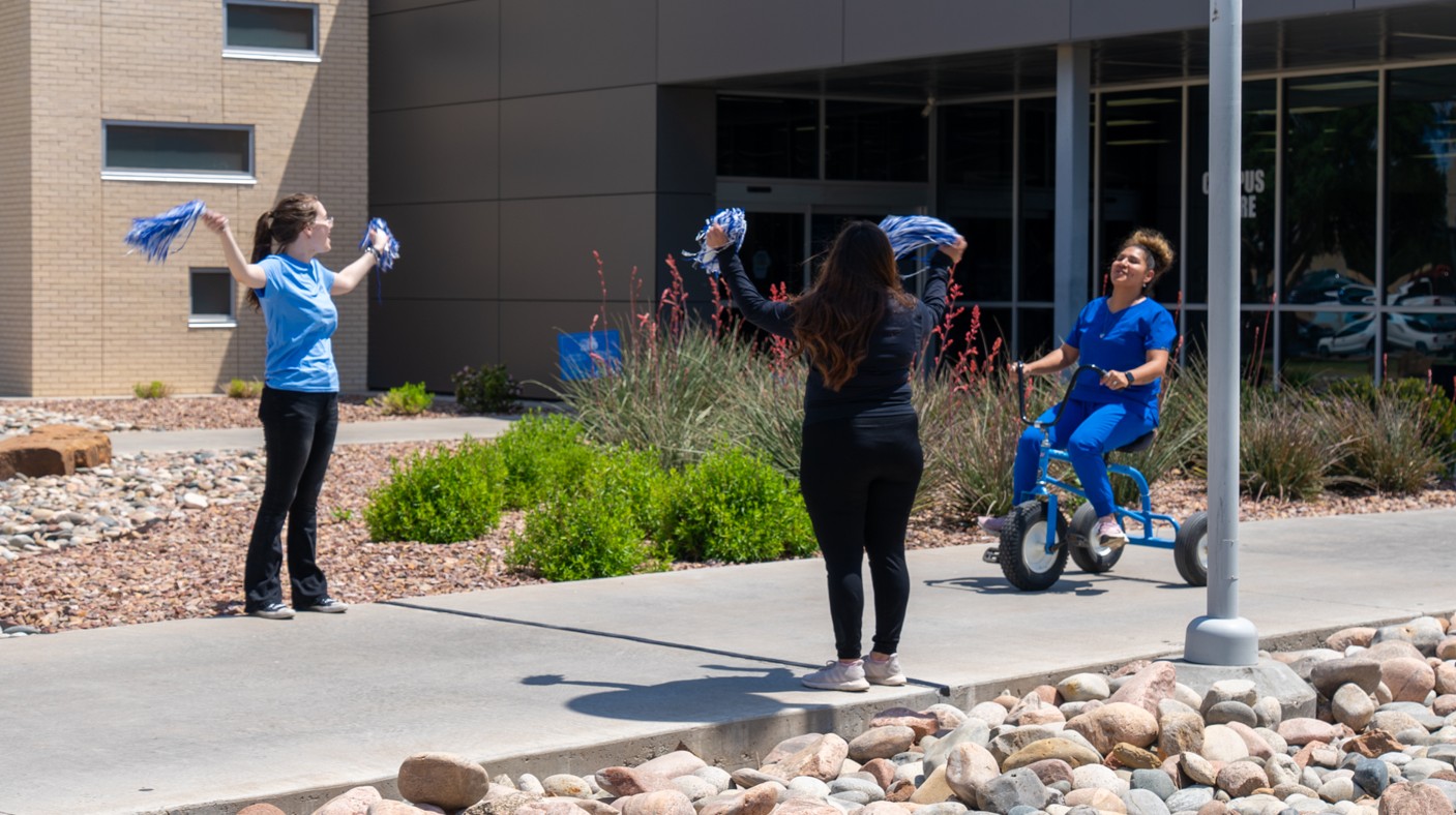 2 girls cheering on someone riding an adult tricycle